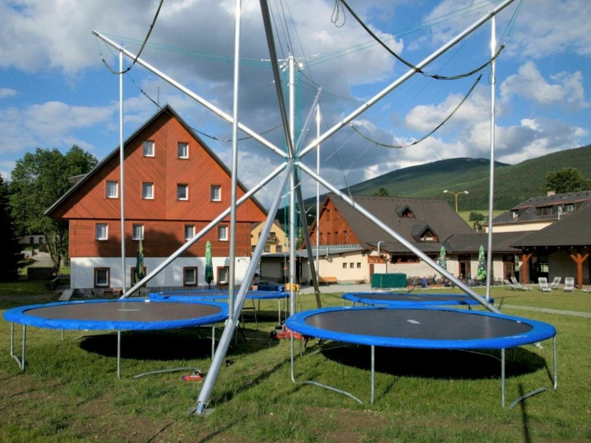 Um edifício com fachada vermelha e várias janelas, rodeado por uma área ajardinada com duas trampolins.