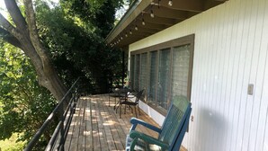 A wooden deck with a rocking chair and a table, surrounded by trees.