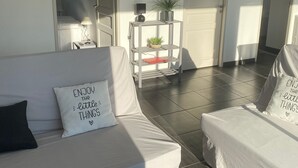 Ein moderner, gut beleuchteter Raum mit einem weißen Sofa, einem kleinen Beistelltisch und einem Regal mit Pflanzen.