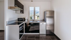 Eine moderne Küche mit Einbauofen, Mikrowelle und Geschirrspüler, einem Edelstahlkühlschrank und einem Fenster mit Blick auf die Berge.