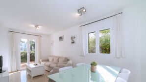 En moderne stue med et glasbord, hvide møbler, en sofa og et fjernsyn.