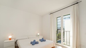 Et soveværelse med seng, to sengeborde, et natbord, en balkon med udsigt og en skydedør af glas.