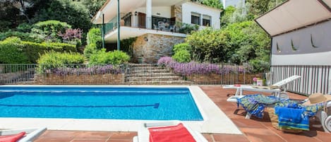 A swimming pool with two sun loungers, one with a red towel.