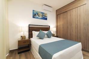 A neatly made bed with a blue blanket, two bedside lamps, and a wall-mounted air conditioner.
