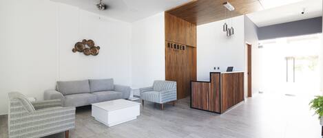 A modern hotel lobby with a grey sofa, striped armchairs, a white coffee table, and a reception desk.