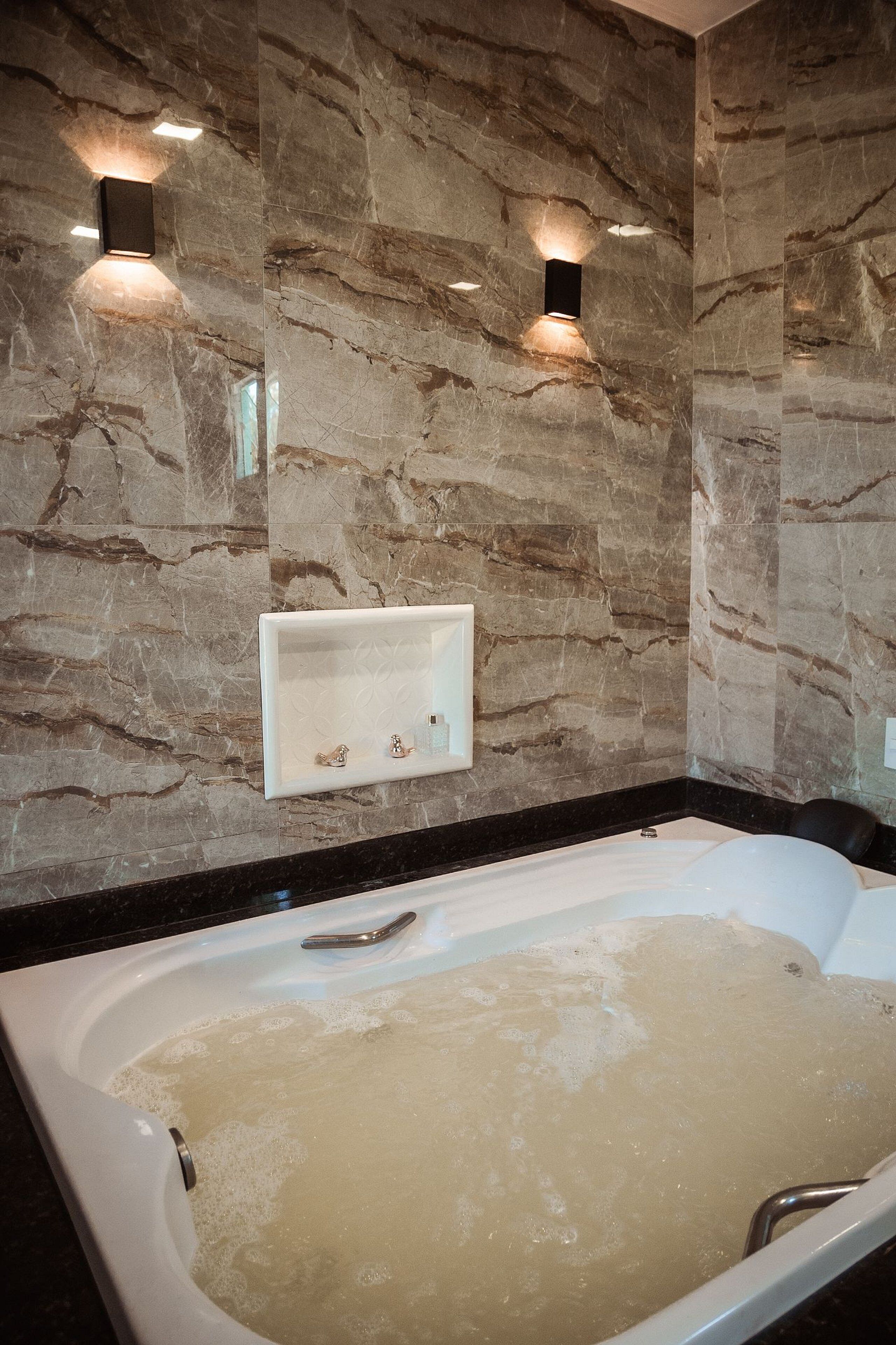 Un baño con pared de mármol, una bañera blanca y dos luces empotradas.