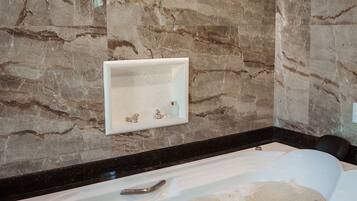 Un baño con pared de mármol, una bañera blanca y dos luces empotradas.