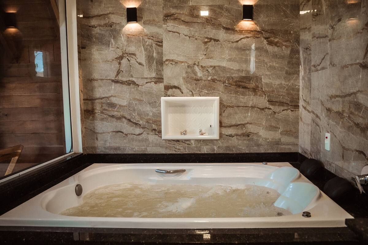 A modern bathroom with a marble wall, a built-in sink, and a bathtub filled with water.