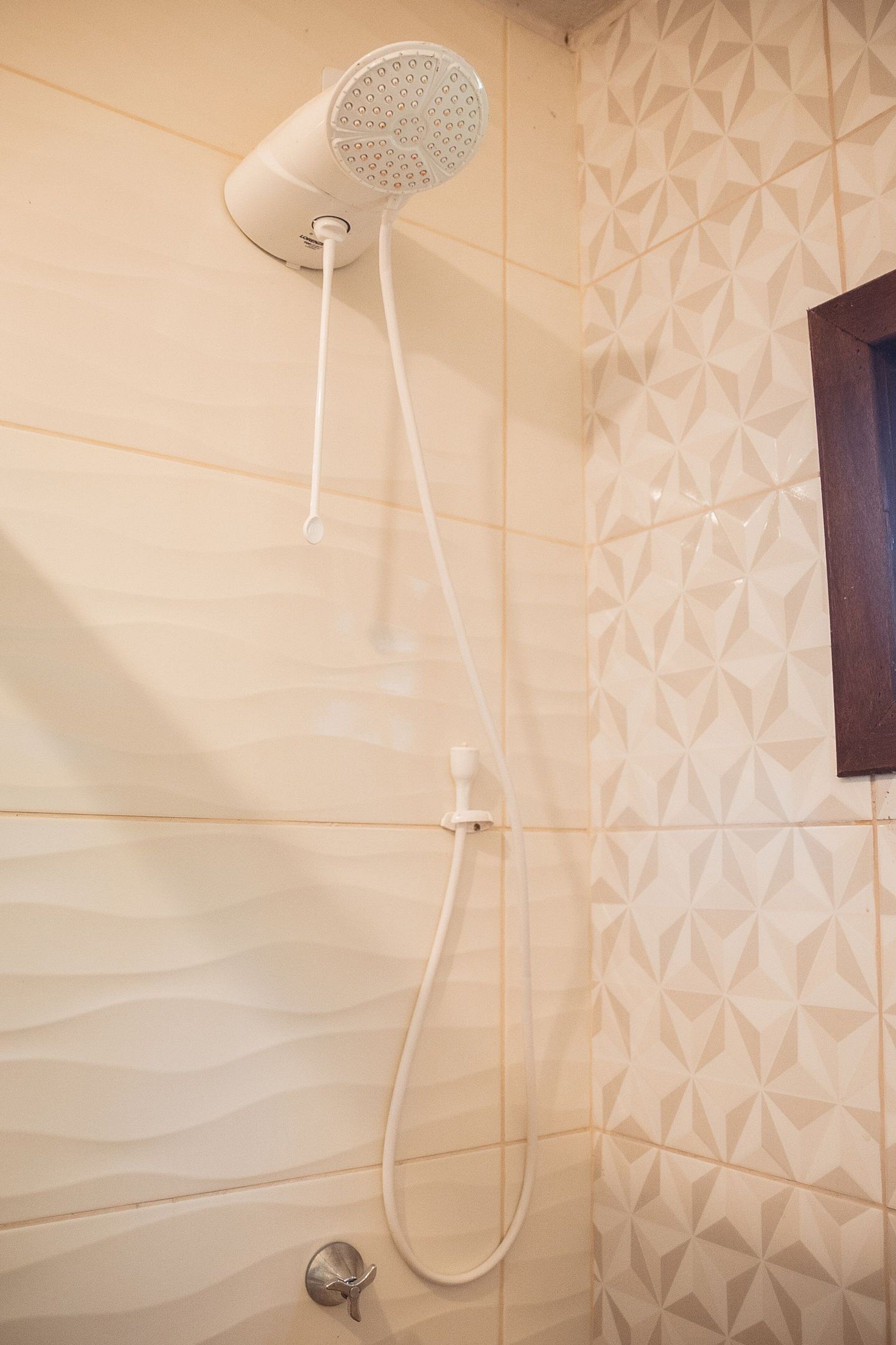 A shower with a handheld attachment, a wall-mounted control panel, and a geometric tile pattern on the wall.