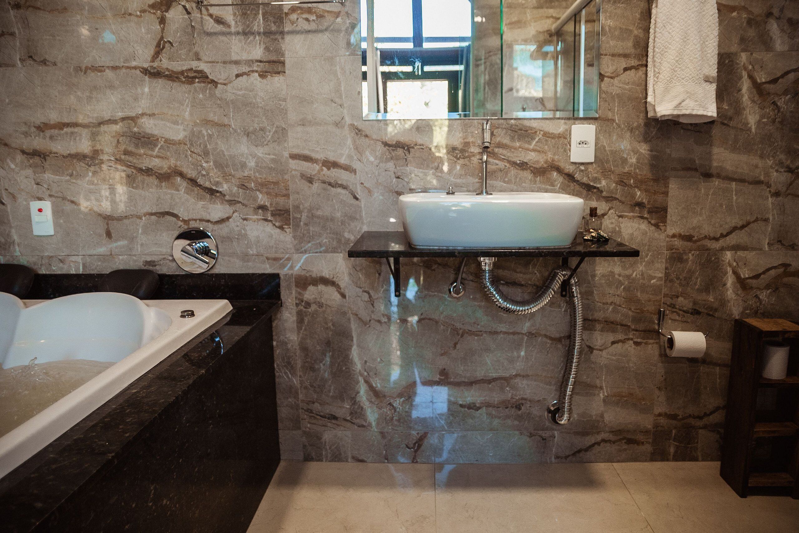 Un baño con pared de mármol, un lavamanos blanco, una bañera y un perchero para toallas.