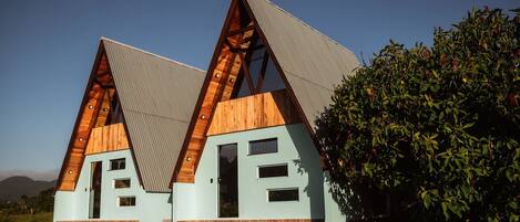 Un edificio moderno de forma triangular con fachada de madera y techo metálico, rodeado de grava y vegetación.