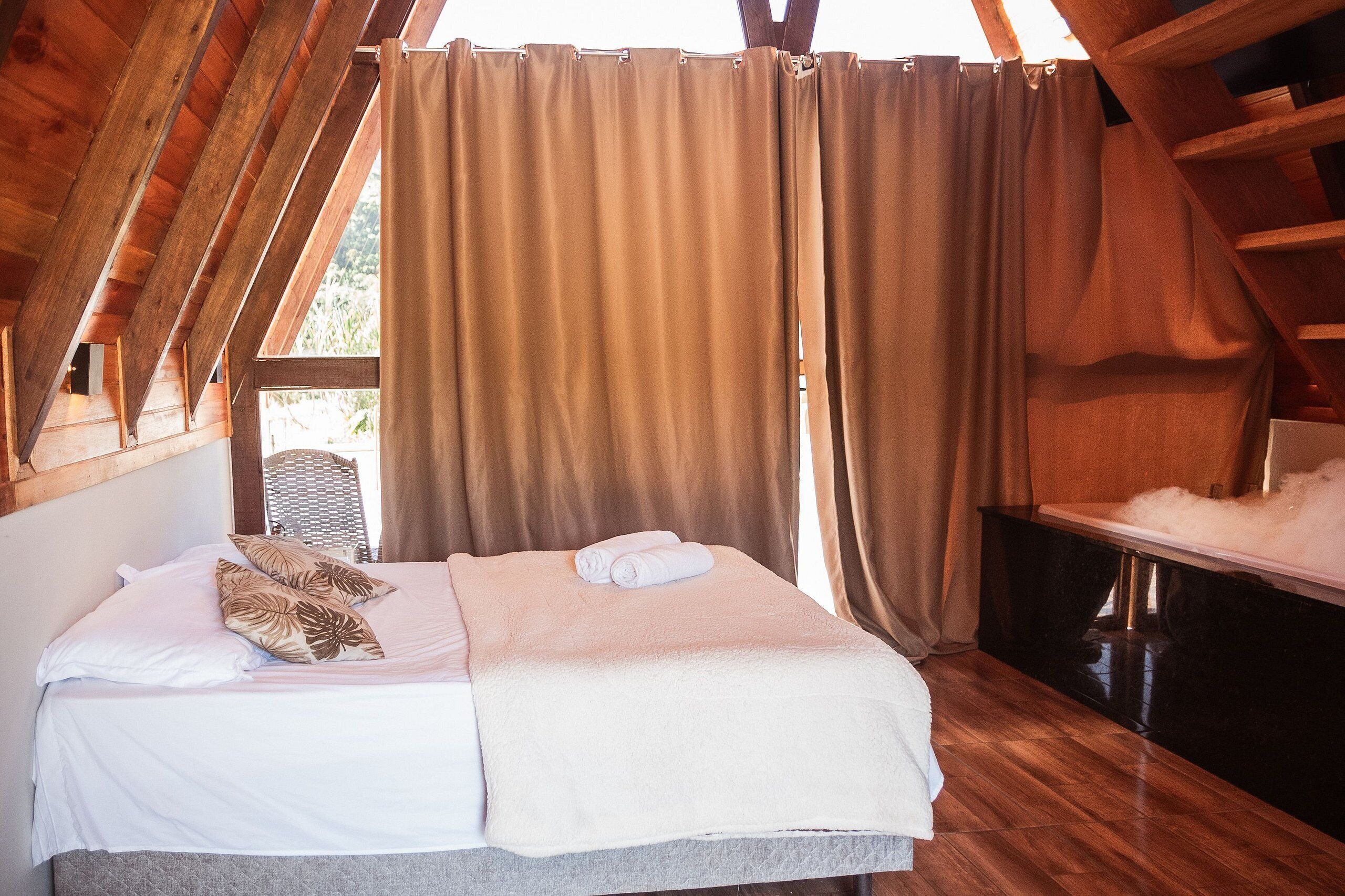 A cozy bedroom with a bed, pillows, and a large window with curtains.