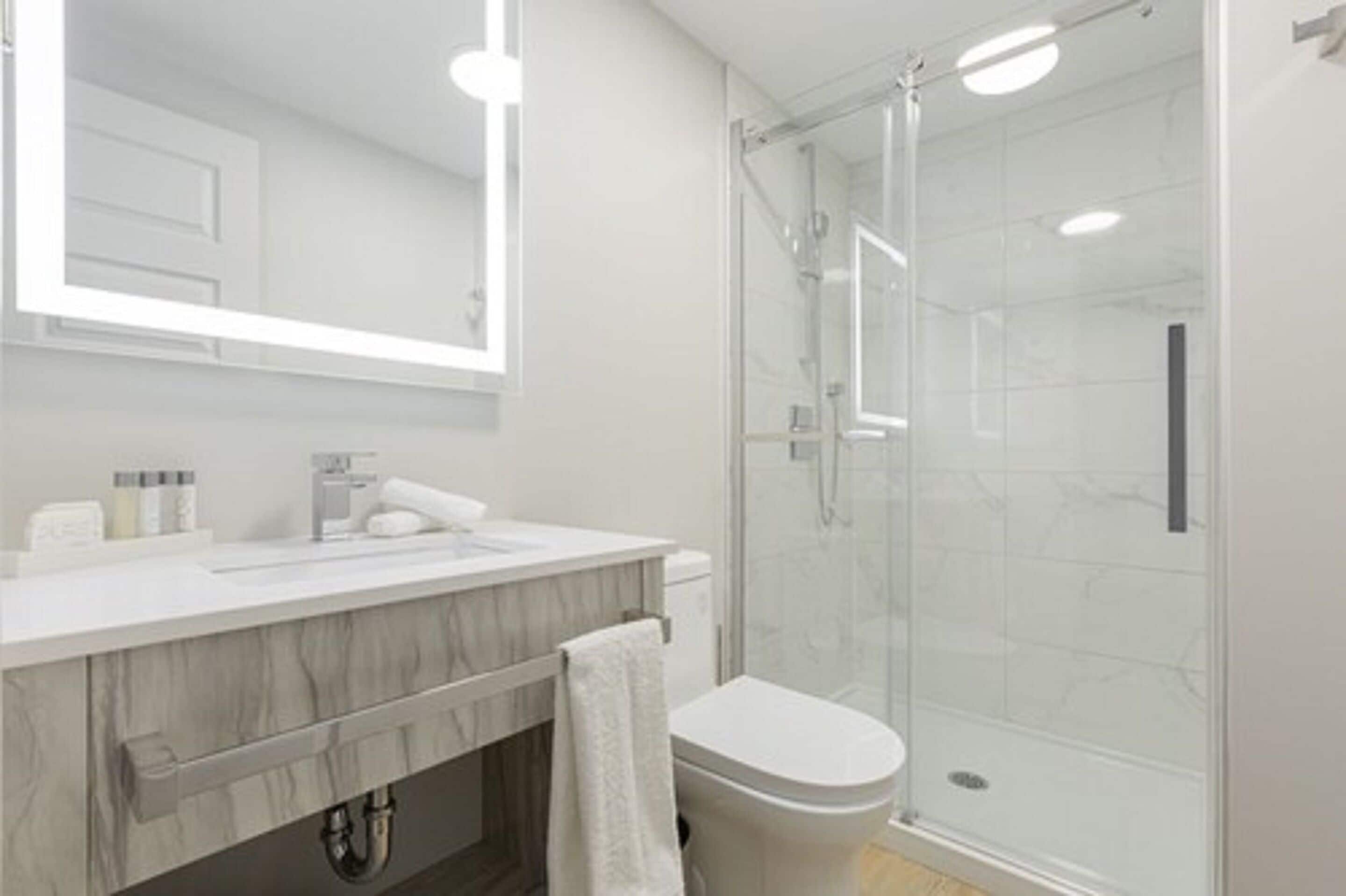 A modern bathroom with a glass shower enclosure, a marble vanity, and a large mirror.