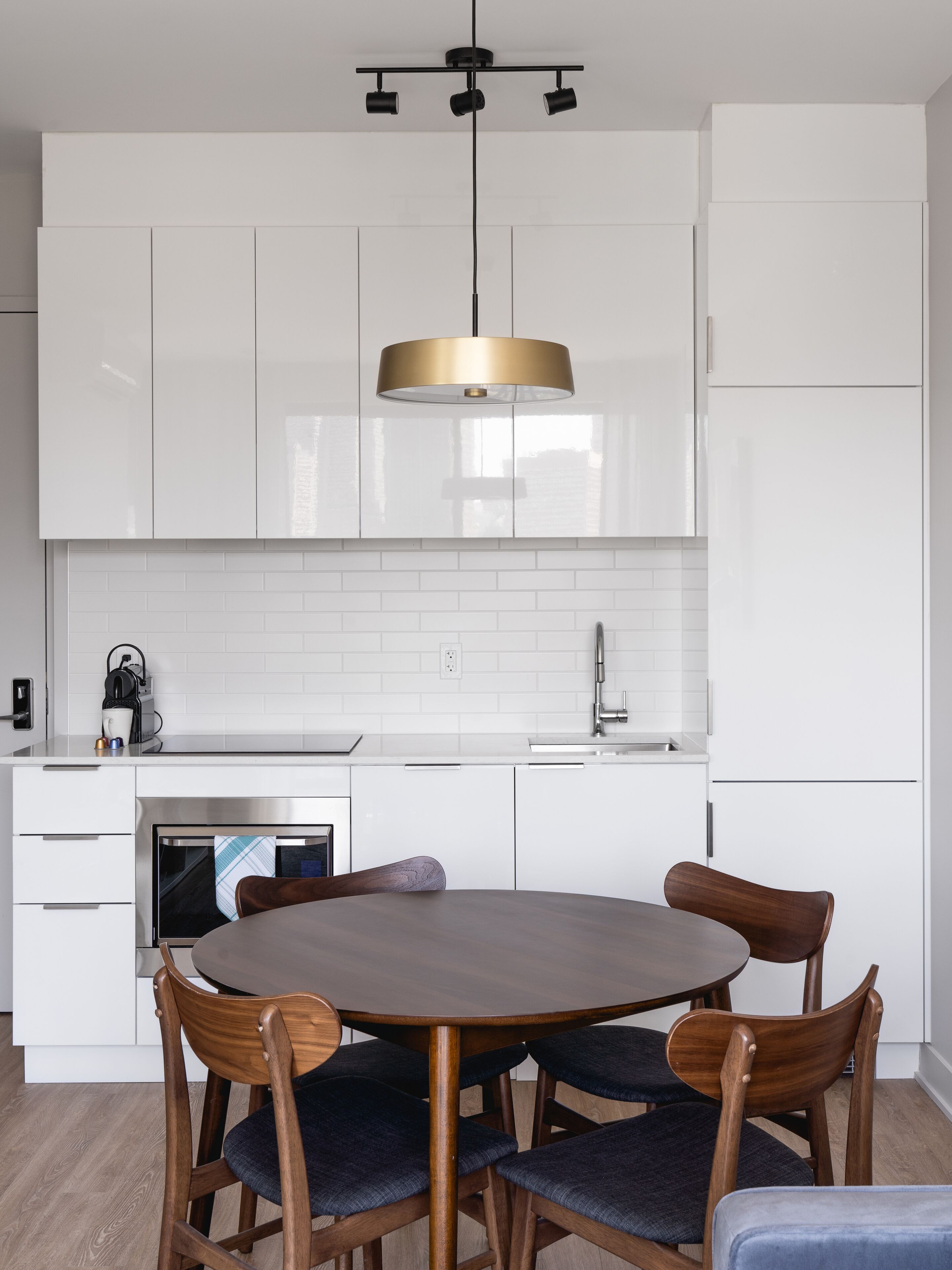 Una cocina moderna con armarios blancos, una mesa redonda de madera y una lámpara colgante.