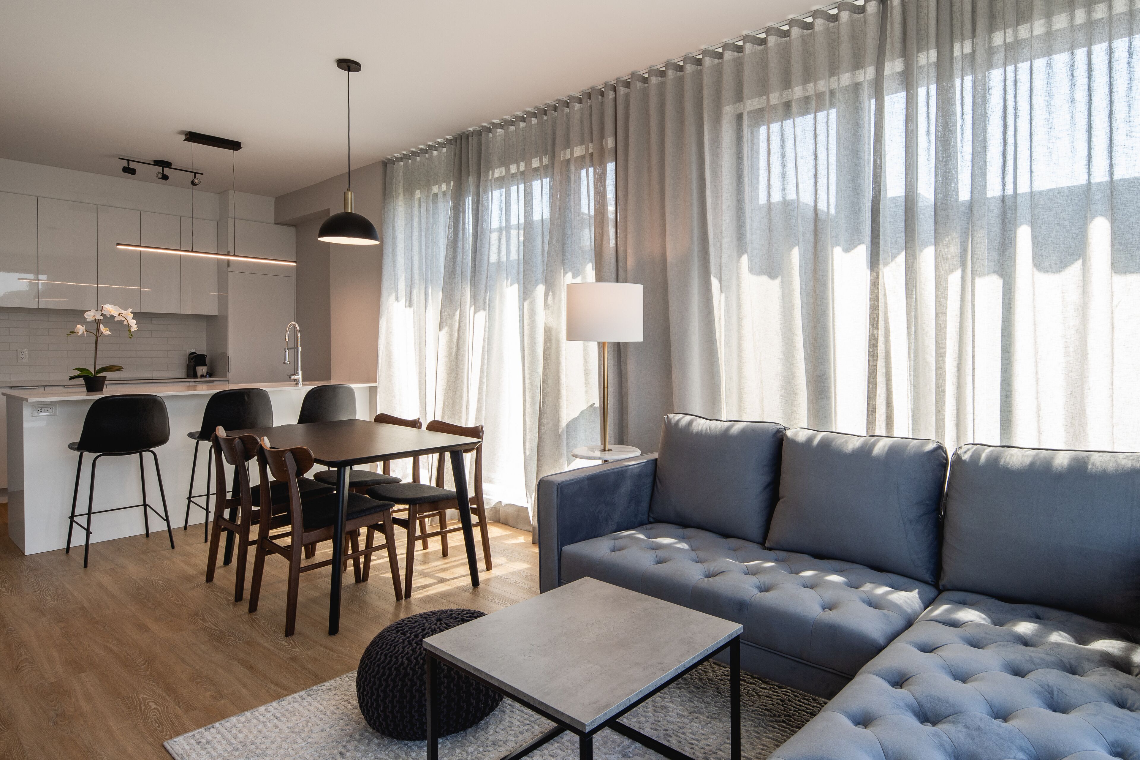 A modern living room with a sofa, dining table, chairs, and a kitchen area.