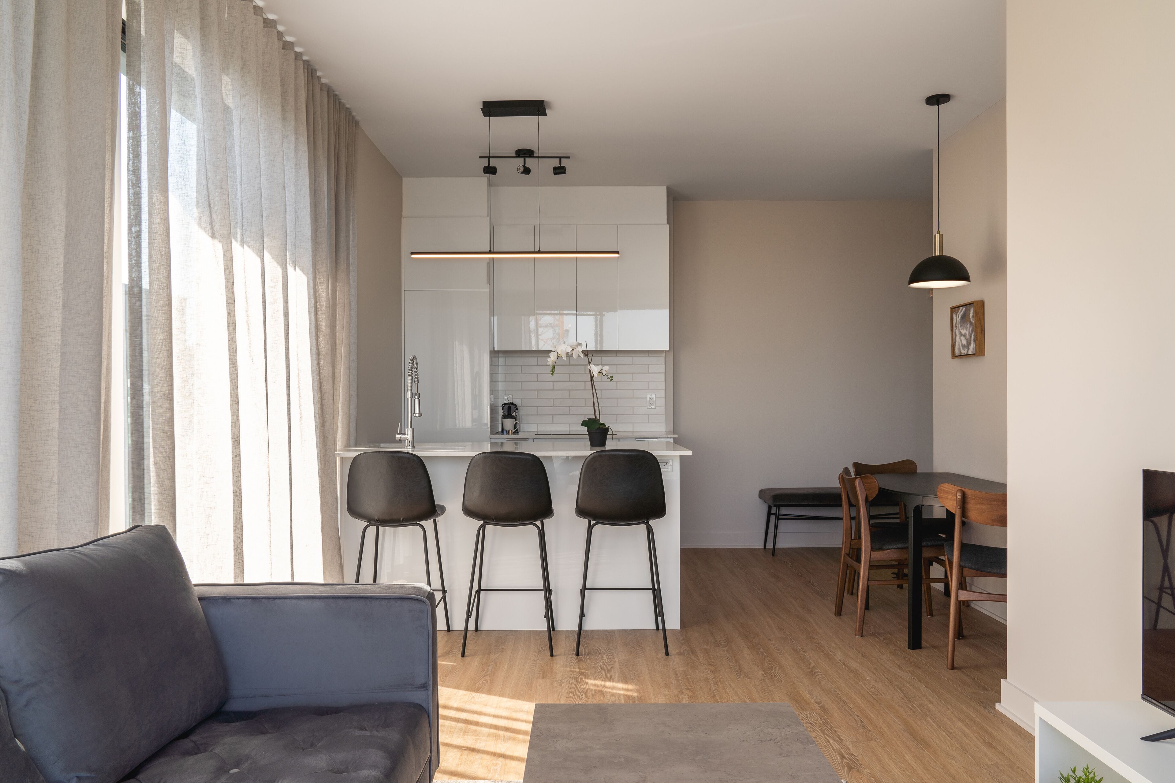 Eine moderne Küche mit weißen Schränken, einer zentralen Kochinsel mit Barhocker und einem Essbereich mit Holzkästen.