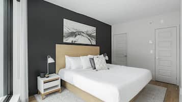 Een moderne slaapkamer met een groot bed, een nachtkastje met een lamp, een schilderij aan de muur en een deur aan de rechterkant.