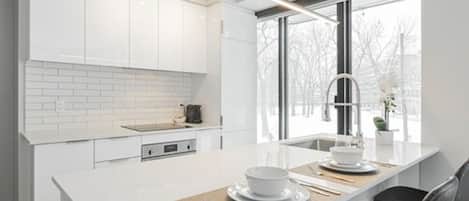 Una cocina moderna con armarios blancos, una isla grande con pileta y vista al exterior a través de un ventanal.