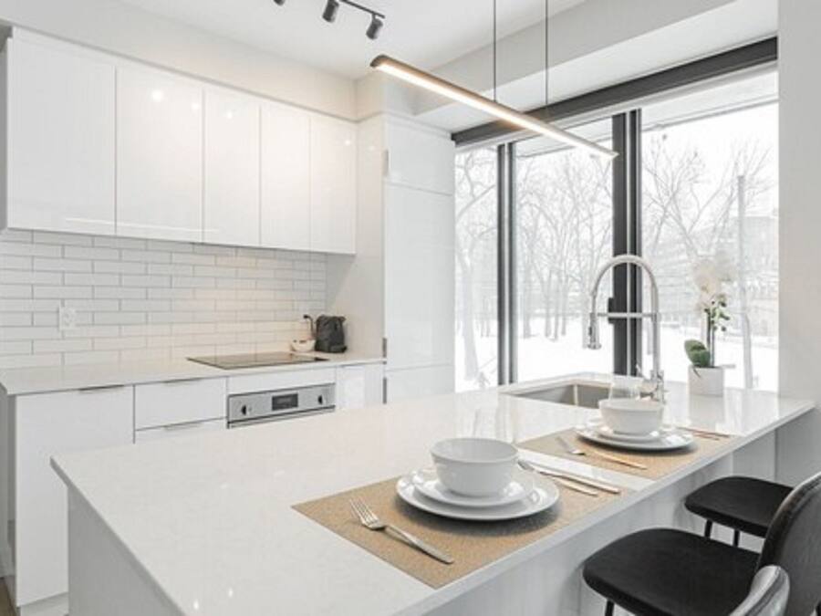 A modern kitchen with white cabinetry, a large island with a sink, and a view of the outside through a large window.