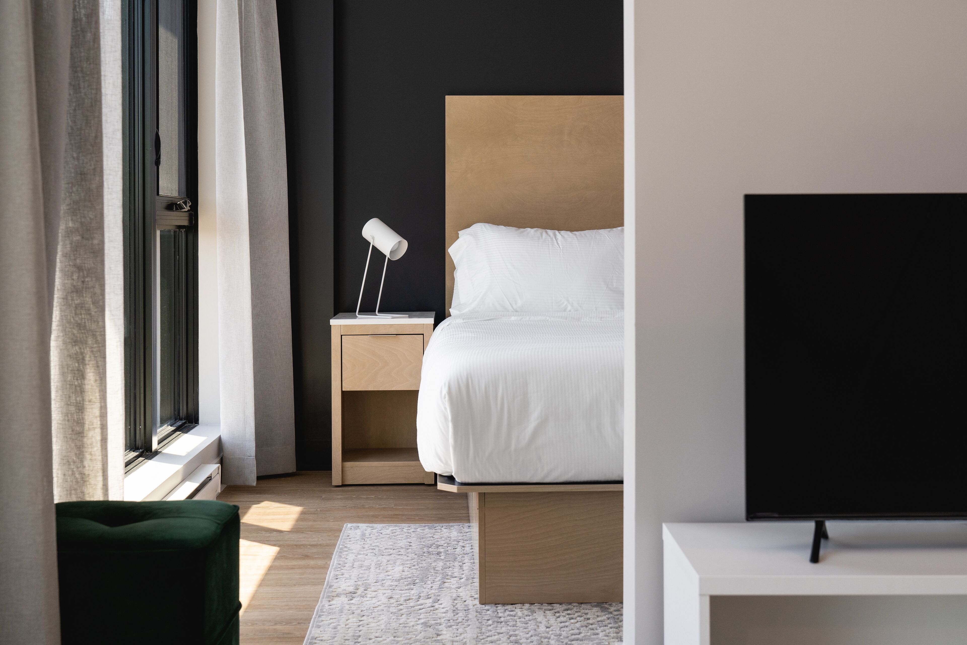 A modern bedroom with a bed, bedside table, lamp, and a TV.