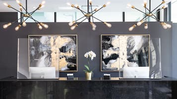 A reception desk with two large abstract paintings, a potted orchid, and a modern chandelier.