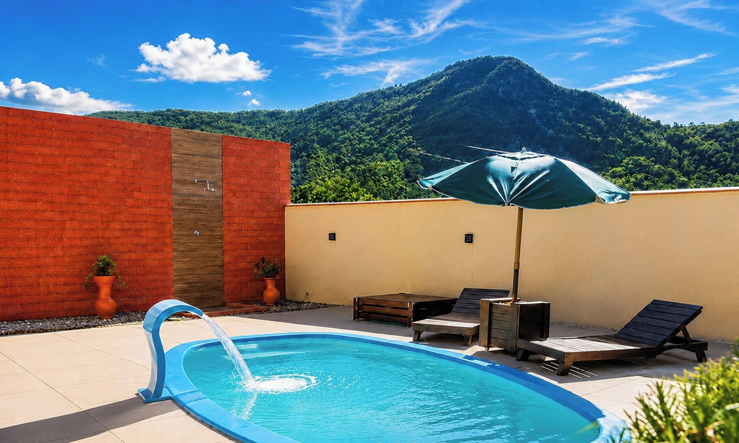 A swimming pool with a water feature, two lounge chairs, an umbrella, and a mountain view in the background.