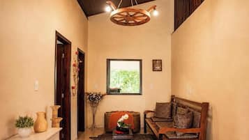 A cozy living room with a wooden ceiling fan, a sofa with patterned cushions, a small side table, and a window with a view of greenery.