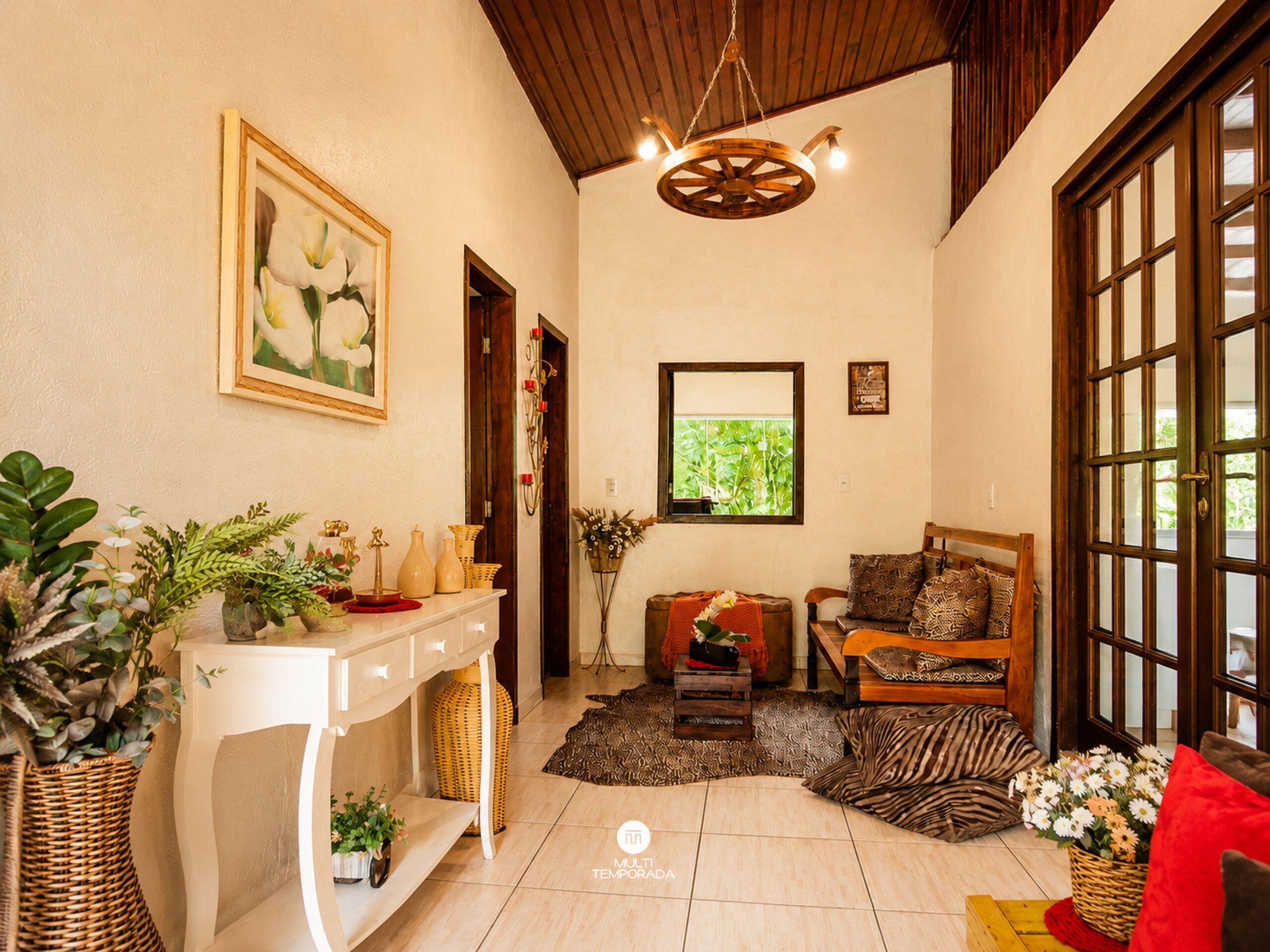 Um quarto com um console branco, um banco de madeira, um tapete estampado e uma janela grande com vegetação lá fora.
