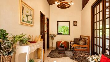Um quarto com um console branco, um banco de madeira, um tapete estampado e uma janela grande com vegetação lá fora.