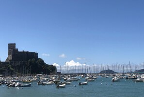 A marina with numerous boats docked, a historic building in the background, and clear skies.