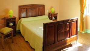 Un dormitorio con cama de madera, una mesita de noche con lámpara, una silla y una pequeña mesa con lámpara.