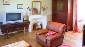 Una sala de estar con un sofá de cuero marrón, una mesa de centro de madera, una chimenea blanca, un televisor y una radio.