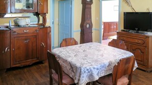 Un comedor con una mesa y sillas de madera, un reloj en la pared y un televisor sobre un mueble.