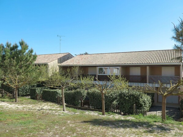 A two-story building with a tiled roof, surrounded by trees and a fence.