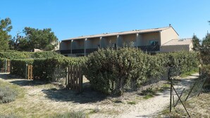 A two-story building with a tiled roof, surrounded by a fence and vegetation. - Cosy apartment for 6 guests with TV, terrace and pets allowed (Carcans-plage)