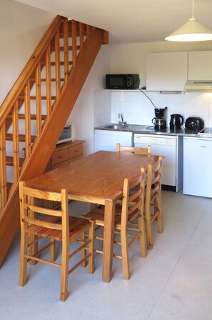 A kitchen with a wooden table and chairs, a microwave, a coffee maker, and a dishwasher. - Cosy apartment for 6 guests with TV, terrace and pets allowed (Carcans-plage)