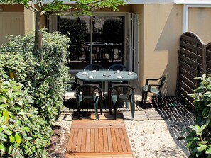 A patio with a table and chairs, surrounded by greenery and a wooden deck. - Cosy apartment for 6 people with TV, terrace and pets allowed (Carcans-plage)