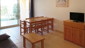Una habitación con una mesa de comedor de madera, sillas, un banco, un sofá, un televisor sobre un mueble de madera y un ventanal con vistas a zonas verdes.