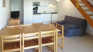 Un comedor con mesa y sillas de madera, una cocina con armarios y electrodomésticos blancos, y un sofá gris.