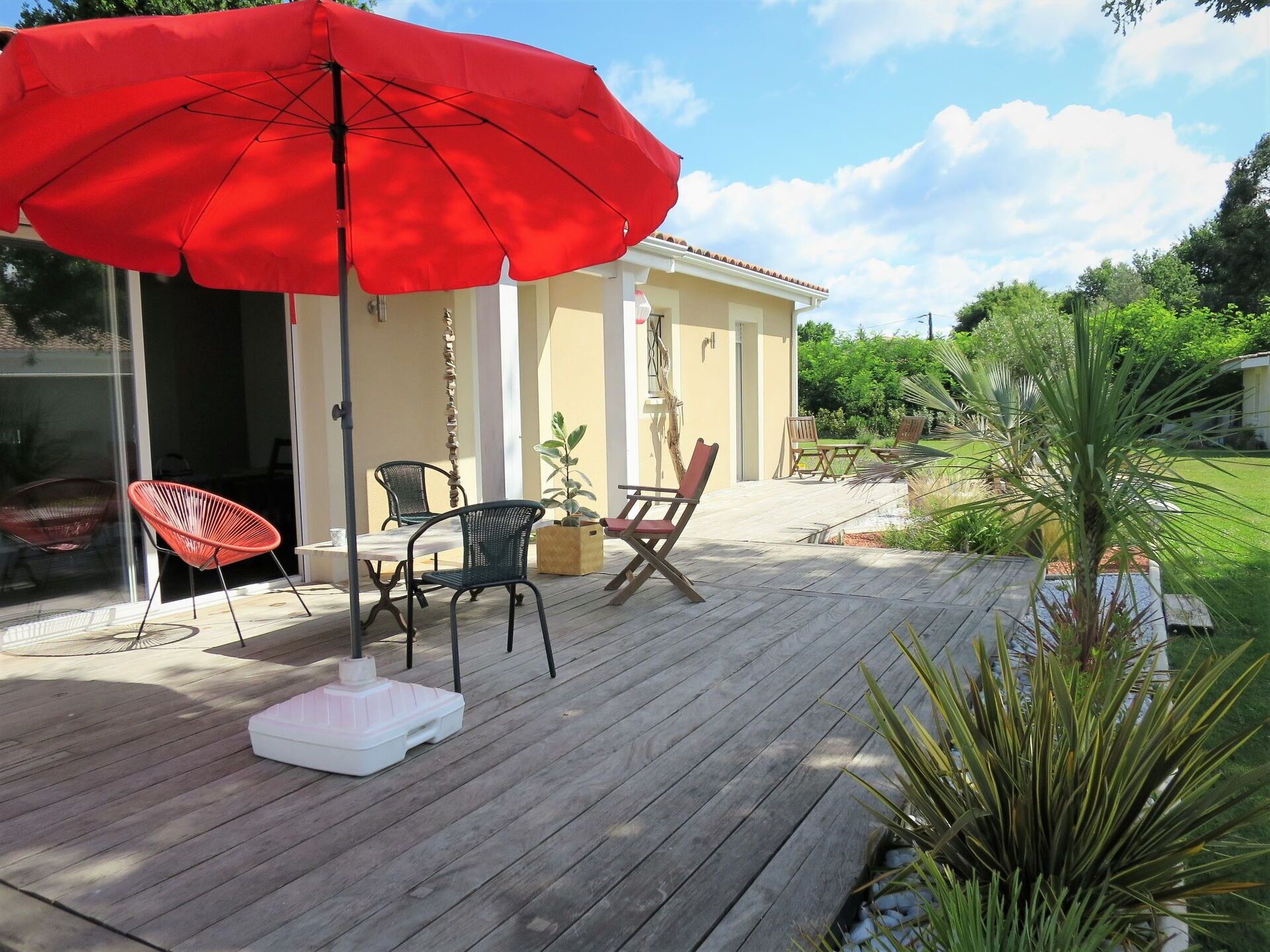 Un patio al aire libre con cubierta de madera, un paraguas rojo y varias sillas.