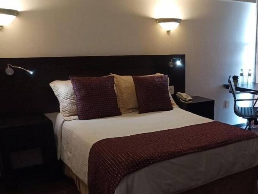 A hotel room with a large bed, two bedside tables, a nightstand, and a chair.