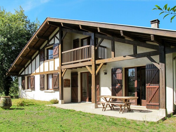 A two-story building with a balcony, wooden doors, and a patio with a table and chairs.