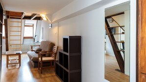 Un salon chaleureux avec un plancher en bois, un canapé, une table basse et une bibliothèque. On peut également apercevoir une échelle et une fenêtre.
