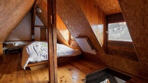 Une petite chambre mansardée avec un plafond en pente, des murs en bois, un lit simple et une fenêtre.