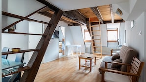 Une pièce de style loft avec des poutres en bois apparentes, une table en bois, un canapé et une échelle.