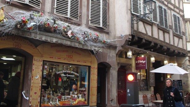 Un bâtiment doté de nombreuses fenêtres et volets, une devanture de magasin avec une enseigne indiquant qu’il s’agit d’une boutique spécialisée, et un piéton qui passe.