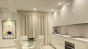 Una cocina moderna con armarios blancos, una mesa de vidrio con cuatro sillas, una cafetera y un horno empotrado.