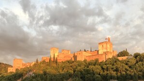 Un castillo histórico con múltiples torres y una bandera en la cima, rodeado de abundante vegetación.