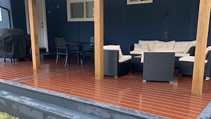 A covered outdoor seating area with a table and chairs, a covered porch with a wooden beam structure, and a dark blue wall with a window. -  NEAR UO, NEW RENO, SLPS 8, PET STAYS FREE, DECK/GRILL, FENCED YARD, VERY CLEAN
 (Eugene)