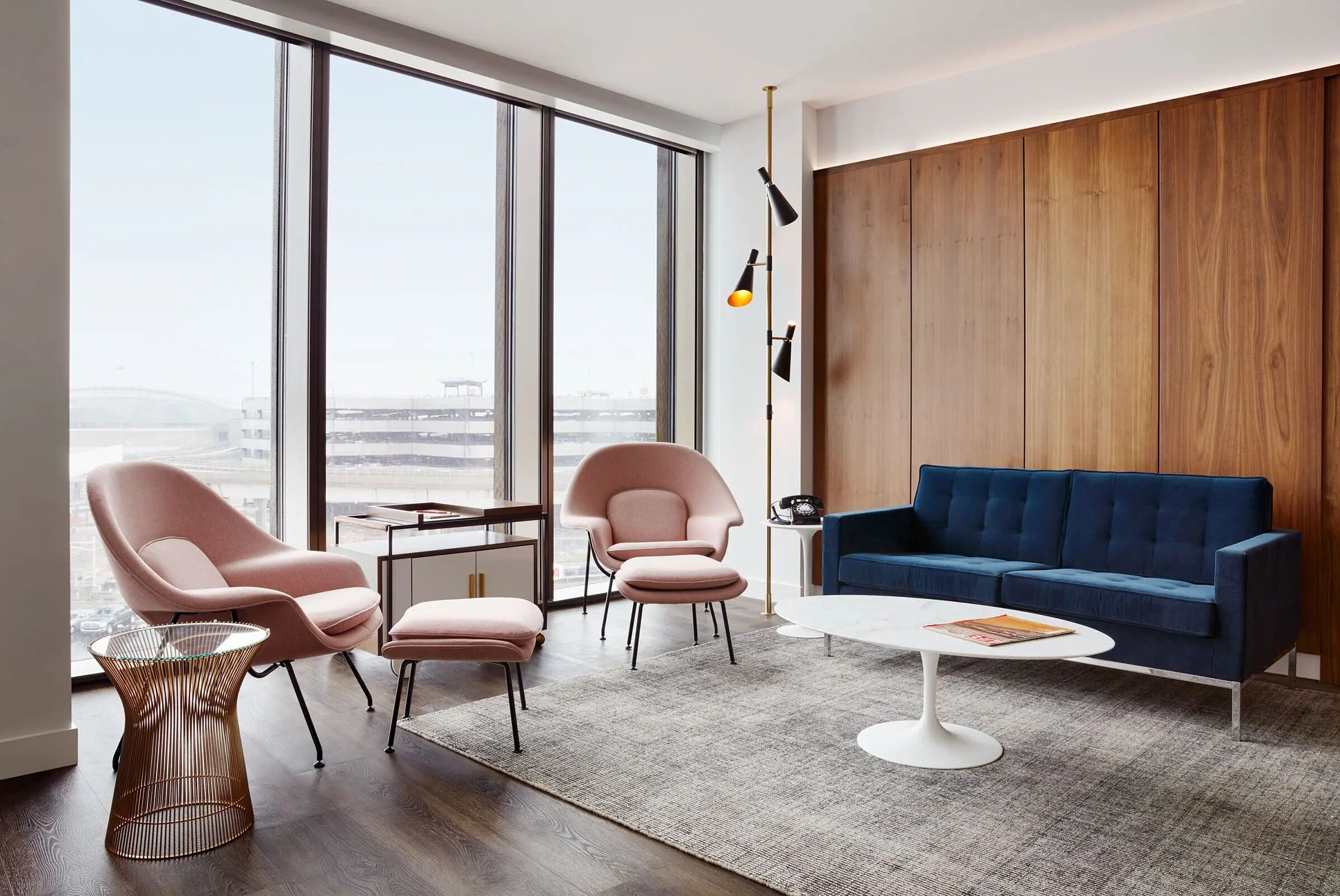 A modern living room with a large window, two pink chairs, a blue sofa, and a white coffee table.